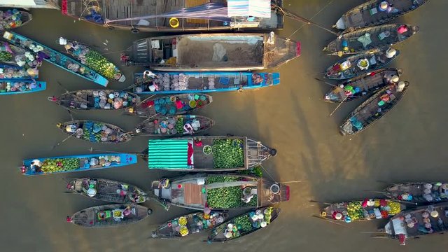 AERIAL, TOP DOWN: Flying away from people selling produce from wooden boats floating around the tranquil murky delta in the Vietnamese countryside. Scenic shot from above of a bustling floating market