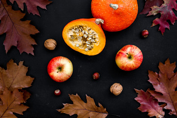 Autumn background. Dried leaves, pumpkin, apple and nuts on black background top view