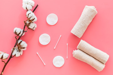 Products made of cotton. Bath accessories. Towels, cotton pads and swabs near dry cotton flowers on pink background top view