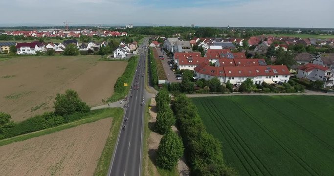 Drohnenaufnahme - autofreie Landstraße mit Radfahrern und Schwenk auf Wohnsiedlung