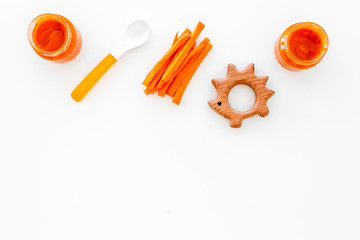Healthy food for small babies. Carrot puree in bowl near carrot slices, spoon, toy on white background top view copy space