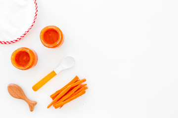 Healthy food for small babies. Carrot puree in bowl near bib, carrot slices, spoon on white background top view copy space