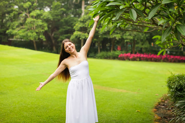 portrait of carefree young woman in white dress posing in green summer park