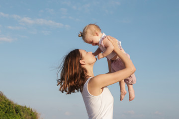 Mother throwing up an adorable baby girl against the clear blue sky, spending together time...