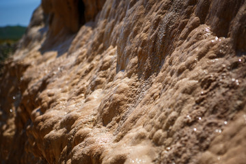 Texture yellow and beige wet uneven bumpy stone glitters in the sun. Calcium stalagnate growths, waterfall mountain in Georgia on the Georgian military road, Golden mountain.