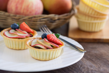 Homemade bakery apple caramel tart decorated with sliced apple strawberry and blueberry on white plate put on wood table. Delicious and sweet pastry ready to served for coffee break or afternoon tea.