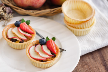 Homemade bakery apple caramel tart decorated with sliced apple strawberry and blueberry on white plate put on wood table. Delicious and sweet pastry ready to served for coffee break or afternoon tea.