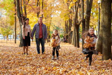 Happy family is in autumn city park. Children and parents running with leaves.. They posing, smiling, playing and having fun. Bright yellow trees.