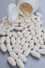 Medicine tablets or pills spilled from fallen pill bottle on gray background. Pharmacy and healthcare concept.