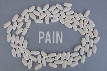 Circle of white medicine tablets or pills on silver color background with word pain in middle.  Pharmacy and healthcare