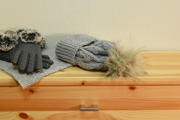 Winter accessories hat with artificial fur pompom, gloves and knitted scarf on wooden shelf with copy space for text.