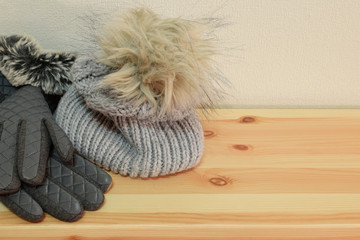Winter accessories hat with artificial fur pompom, gloves and knitted scarf on wooden shelf with copy space for text.