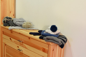 Winter accessories hat with artificial fur pompom, gloves and knitted scarf on wooden shelf with copy space for text.