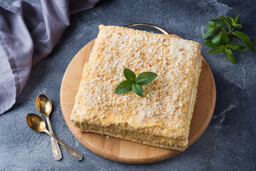 Layered cake with cream Napoleon millefeuille vanilla slice with mint on dark background.