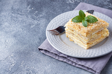 Layered cake with cream Napoleon millefeuille vanilla slice with mint on dark background.