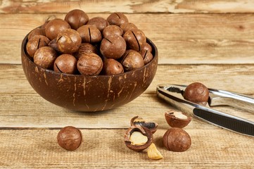 Macadamia nuts in the brown bowl and nutcracker on wooden table, close-up