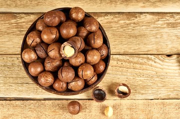 Macadamia nuts in the brown bowl on wooden table, flat lay