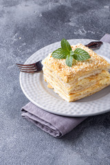 Layered cake with cream Napoleon millefeuille vanilla slice with mint on dark background.