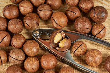 Macadamia nuts and nutcracker on wooden table, close-up