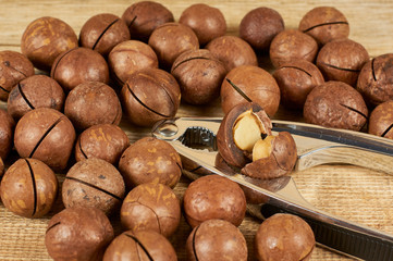 Macadamia nuts and nutcracker on wooden table, close-up