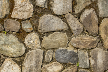 a wall of various large natural stones. wall with moss. rough wall surface texture. gray, blue and white stones.