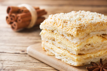 Layered cake with cream Napoleon millefeuille vanilla slice with cinnamon and anise on wooden background.