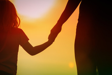 silhouette of mother and daughter holding hands at sunset