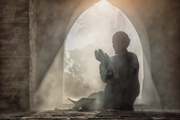 Silhouette of muslim male praying in old mosque with lighting and smoke background
