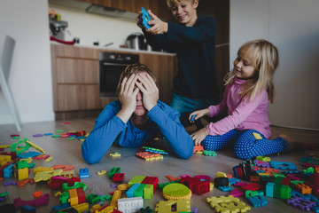 kis play with toys scattered all over and tired exhausted father