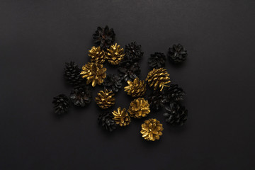 Pine cones painted in golden, black colors, Christmas-tree decorations on a black background. Minimalism. Concept of Happy New Year and Merry Christmas. Flat lay, top view