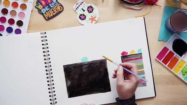 Step by step. Flat lay. Baker sketching a design of a cake with watercolors for Dia de los Muertos holiday.