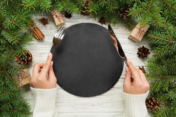 top view girl holds fork and knife in hand and is ready to eat. Empty black slate plate on wooden...