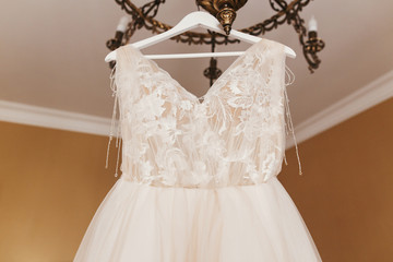 Stylish Wedding dress. Modern wedding gown hanging on chandelier in room. Space for text. Bride accessory for wedding. Wedding salon or showroom
