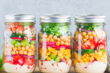 Fototapeta na wymiar Glass jars with layering various vegan salads for healthy lunch. The concept of fitness and vegetarian food.