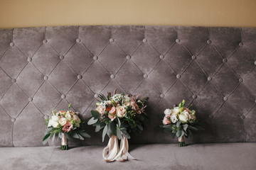 Modern wedding bouquets of pink roses and green eucalyptus with pink ribbons on stylish grey sofa. Contemporary composition of bridesmaids and bride bouquets on soft fabric
