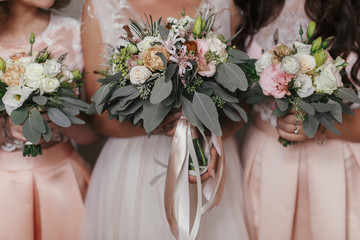 Bridesmaids and bride holding modern wedding bouquets of pink roses and green eucalyptus with pink ribbons. Stylish Contemporary bouquets on soft fabric. Wedding arrangements - obrazy, fototapety, plakaty