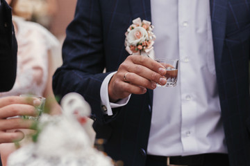 Stylish man holding glasses of vodka and toasting at wedding reception. Corporate businessman...