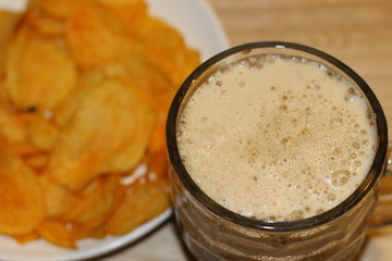 Foamy black beer and crispy chips on white plate