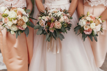 Gorgeous bride and beautiful Bridesmaids holding stylish wedding bouquets on background of modern ...