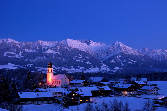 Fototapeta Winter im Gebirge mit Dorf und Kirche zur Abenddämmerung