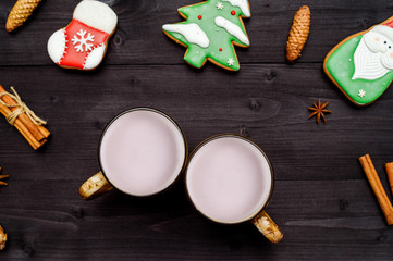 Christmas homemade gingerbread cookies with icing, cinnamon and two mugs of hot cocoa on dark wooden background, top view, flat lay. Santa, fir tree, cinnamon, anise star, copy space
