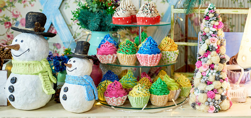 Christmas background with snowman, decorated Christmas tree and colorful cupcakes on wooden table, copy space. Festive snowmen with Christmas decorations