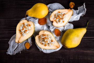 Yellow, ripe pears whole and halves prepared for roasting with cottage cheese, nuts and dried apricots lie on a white napkin on a black wooden table. View from above