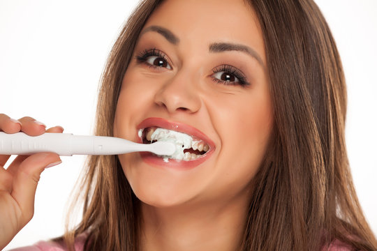young woman brushing her teeth with electric tooth brush on white background