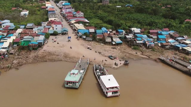 Aerial view circling two Mekong river ferries in Asia as they load and unload passengers and vehicles; other boats and shophouses visible nearby (Speed is x2 for time lapse purposes)
