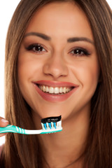 young woman brushing her teeth with black active charcoal toothpaste on white background