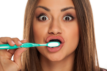 young woman brushing her teeth with black active charcoal toothpaste on white background