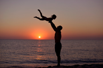 Silhouette of playing dad and daughter on the background of the sea sunset in the summer.