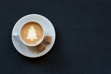 Cup of coffee with milk, cane sugar and christmas tree on dark background. Top view, copy space