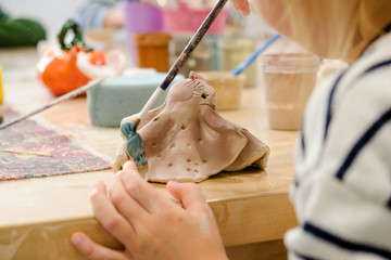 A child paints his clay figurine in a workshop at a modeling lesson.